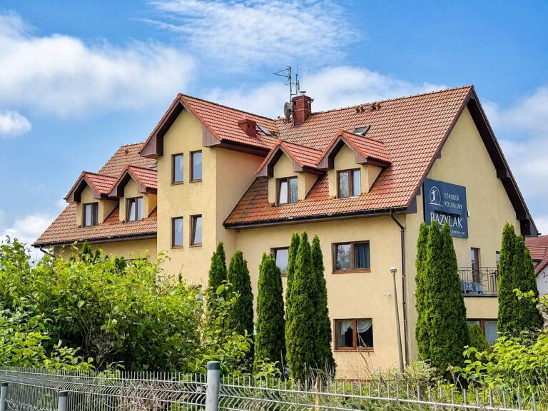 Budynek Ośrodka kolonijnego Bazylak Nad morzem, z zadbaną zielenią i ogrodzeniem, oferujący noclegi dla kolonii, obozów i grup zorganizowanych.